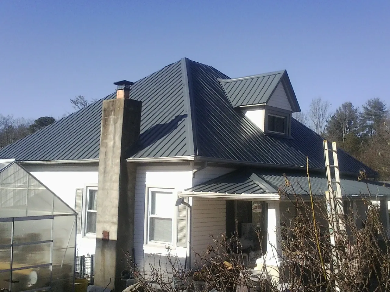 Dark blue standing seam metal roof on a white farmhouse with dormer — Slate & Tile Roof Repair by Roofing Brothers in Collinsville
