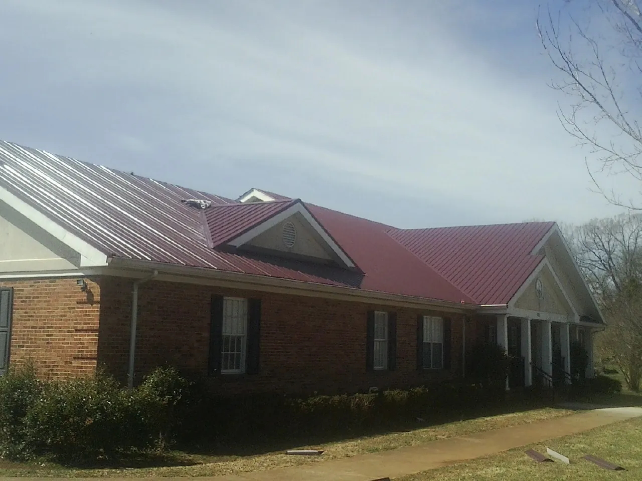 Red metal roof with gabled entries on a long brick building, from a Hail Damage Roof Repair job in Collinsville