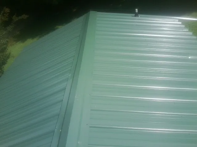 New green metal panels meeting at the ridge of a roof — Flat Roof Repair work by our crew in Collinsville